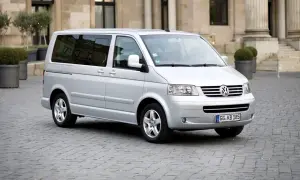 Srebrny Volkswagen T5 na brukowanym placu przed budynkiem z kolumnami.